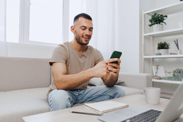 Smiling man using smartphone in modern living room, enjoying connectivity and comfort. A relaxed atmosphere with a cozy interior enhances the experience of technology.