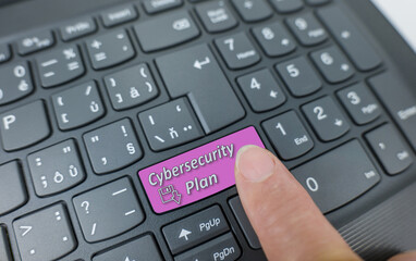 Cybersecurity plan key on a gray keyboard. Finger pressing key