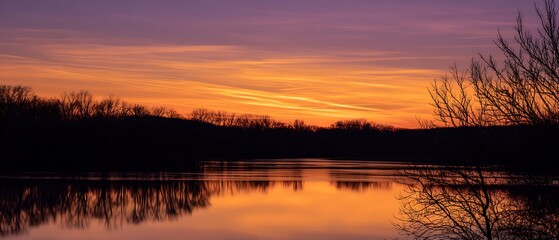 Obraz premium Serene sunset over calm lake with silhouetted trees
