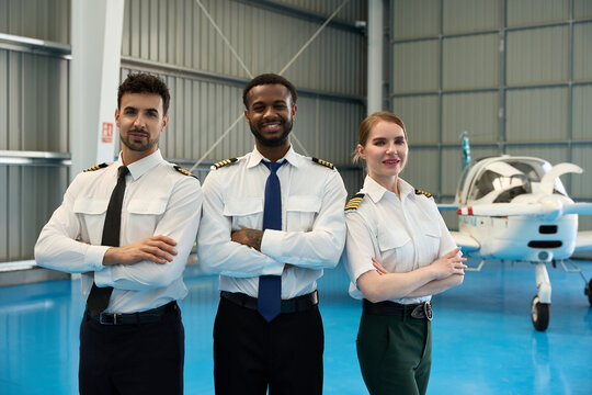 Confident student pilots posing in aircraft hangar
