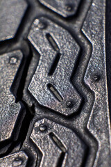 Extreme close-up of a black rubber tire with rugged tread pattern and metallic texture, showcasing deep grooves, surface wear, and tire design details