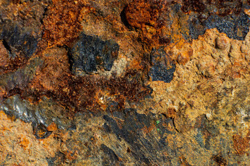 Close-up of rusty oxidized metal with textured stone surface, colorful corrosion details with orange, black, and brown patterns, industrial decay concept