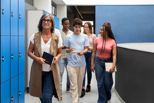 Teacher and high school students walking in school corridor - Powered by Adobe