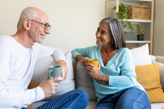 Mature couple relaxing sitting on the couch, talking while having coffee. Happy married couple having conversation.