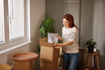 Woman is unpacking her belongings in a newly moved-in living area, arranging items from boxes in a...
