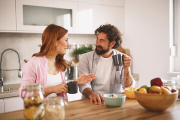 A couple sits at a wooden kitchen table, sharing coffee and laughter. The light fills the bright, modern space as they engage in a warm discussion filled with smiles.