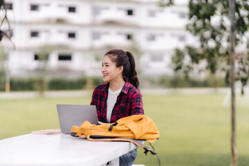 Smiling Asian Woman Studying Outdoors with Laptop
