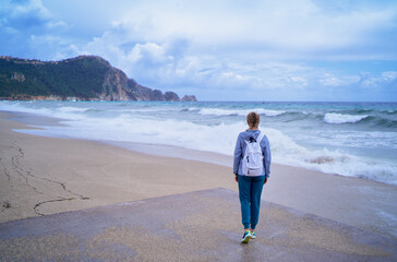Woman Strolling Along a Scenic Beach During a Cloudy Day