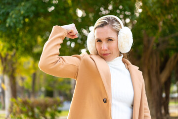 Young blonde woman wearing winter muffs at outdoors doing strong gesture