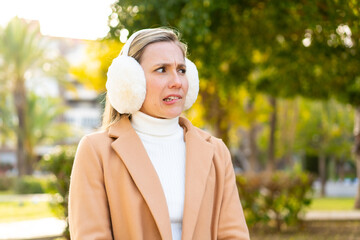Young blonde woman wearing winter muffs at outdoors with confuse face expression