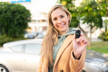 Fototapeta premium Young blonde woman holding car keys at outdoors with happy expression