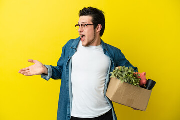 Russian Man making a move while picking up a box full of things isolated on yellow background with...
