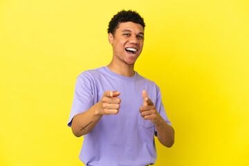 Young African American man isolated on yellow background surprised and pointing front