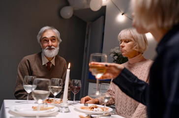 Joyful family reunion at warmly lit dining table, featuring senior adults enjoying dinner, wine, and conversation. To represent togetherness, celebration, and meaningful gatherings with loved ones.