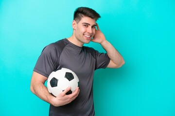 Young caucasian football player man isolated on blue background listening to something by putting...