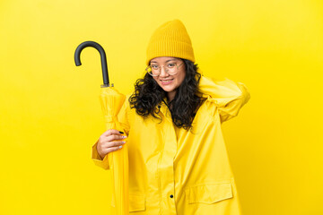 Asian woman with rainproof coat and umbrella isolated on yellow background laughing