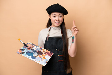 Young Chinese painter woman isolated on beige background showing and lifting a finger in sign of...