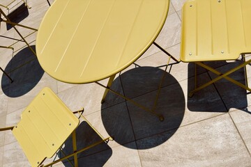 Bright yellow round table and foldable chairs on a terrace in Malta in a play of light and shadow.