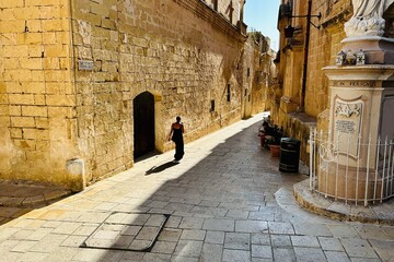 Person female seen from the back unrecognizable walking down a sunny path on the streets of old city