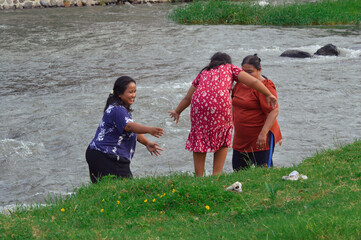 The two mothers carefully help their daughter descend the grassy riverbank as they prepare to enjoy...