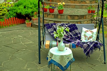 Apple blossoms on a table in front of a sofa swing in the courtyard of a country house.