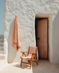 A peach-toned throw hangs beside a wooden chair draped with a matching textile, situated on a sun-drenched patio adjacent to a rustic, peach-colored door set in a whitewashed wall