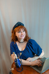 A beautiful young woman is working or playing or shopping on a laptop in a stylish modern dress and a hair band in the shape of the Russian national kokoshnik headdress