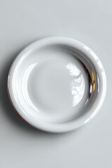 Empty white ceramic plate on light gray background with subtle reflection and shadow detail, minimalist tableware composition for food photography and menu design.