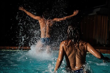 Man jumps into pool splashing women during nighttime fun at a gathering, Man splashing women after jumping in a pool