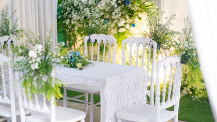 beautifully set table with elegant white chairs and a lace tablecloth, adorned with lush green...