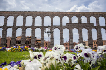 Roman Aqueduct with Flowers in Spain. Beautiful Arch Bridge in Segovia during Cloudy Day.