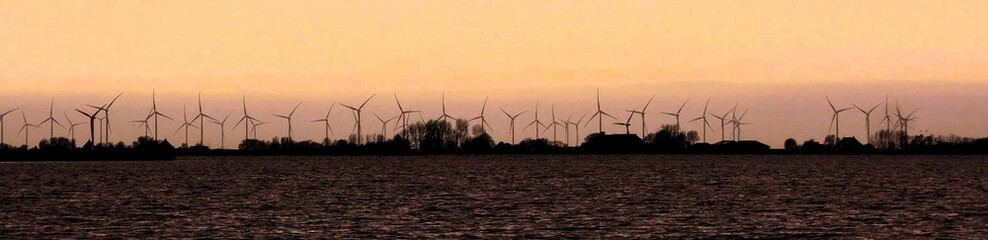 At dusk in Oudega Friesland Netherlands, on the horizon many wind energy turbines. A politically controversial topic
