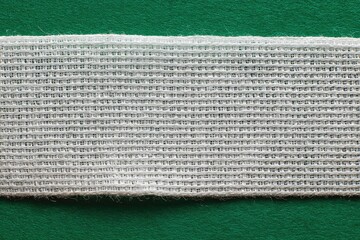 Close-up of a white woven fabric strip on a green background, showing its texture and slightly frayed edges