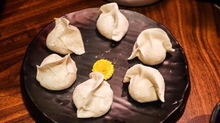 close up of six uncooked raw pork dumplings (Jiaozi or Gyoza) on a plate with a yellow flower in the middle for decoration