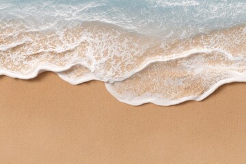 Overhead view of a gentle ocean wave lapping onto a sandy beach; light blue water with white foam contrasting against the tan sand