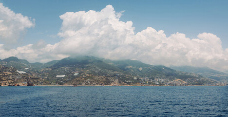 Scenic coastal landscape with blue sea, mountain ridge and dramatic clouds over a Mediterranean town. Summer travel, Clouds descend on the mountains. Panorama seascape with mountains and clouds