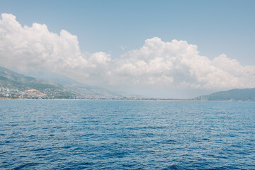 Scenic coastal landscape with blue sea, mountain ridge and dramatic clouds over a Mediterranean town. Summer travel, nature and seascape concept. Clouds descend on the mountains.