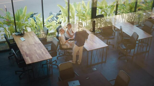 Three colleagues are discussing work in modern coworking space with wooden desks and plants, fostering collaborative and eco conscious environment. Coworking space concept for work