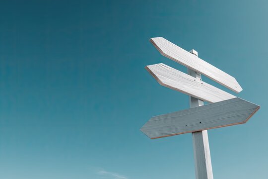 Three blank white wooden directional arrows against a clear teal sky, signifying choices and direction