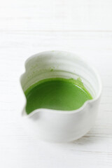 Cup of fresh matcha tea, green tea on white wooden table.