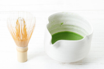 Cup of fresh matcha tea, green tea and Chasen, bamboo whisk, on white wooden table.