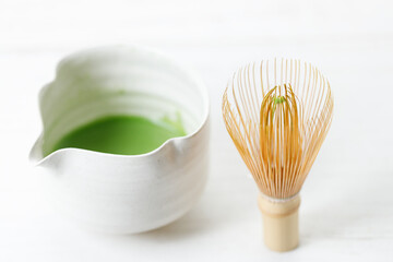 Cup of fresh matcha tea, green tea and Chasen, bamboo whisk, on white wooden table.