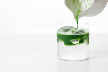 fresh matcha tea, green tea pouring on a glass of coconut water on white wooden table.