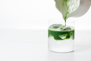 fresh matcha tea, green tea pouring on a glass of coconut water on white wooden table.