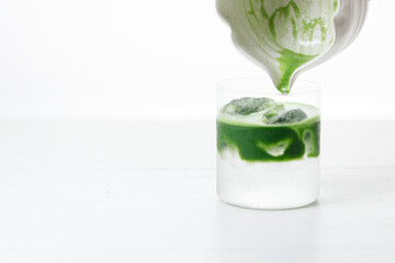 fresh matcha tea, green tea pouring on a glass of coconut water on white wooden table.