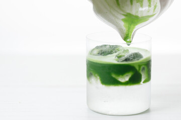 fresh matcha tea, green tea pouring on a glass of coconut water on white wooden table.