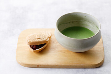 Cup of fresh matcha tea, green tea and Taiyaki, Japanese fish-shaped cake, filled with Anko or red bean on wooden plate.