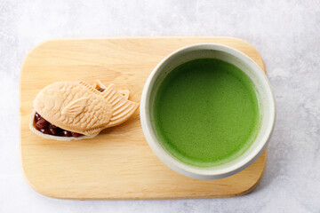Cup of fresh matcha tea, green tea and Taiyaki, Japanese fish-shaped cake, filled with Anko or red bean on wooden plate.