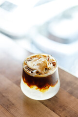 Cup of creation black coffee drink and coconut water decorated with coconut kernel on wooden table by the window.