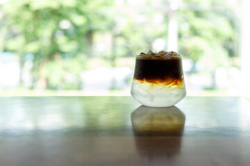 Cup of creation black coffee drink and coconut water decorated with coconut kernel on wooden table by the window.
